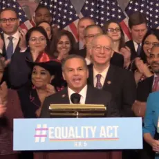 Rep. David Cicilline speaks at a podium with a group of applauding Congresspeople