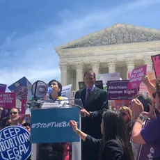 Senator Blumenthal and Representative Chu stand at a podium surround by activists at a #StoptheBans rally