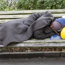 A homeless person naps with their belongings on a bench