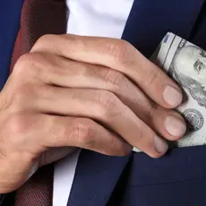 A man puts a $100 bill into his jacket pocket