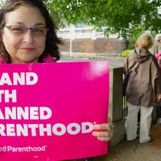 A woman holds a pink sign that says "I stand with Planned Parenthood"