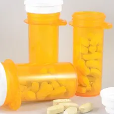 three orange bottles of pills with one opened and one knocked over and pills spilling out