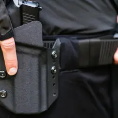 A close up of a police officer's belt; the officer has his hand on his gun