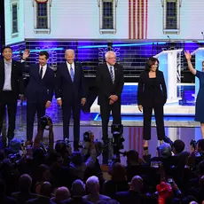 The Democratic presidential candidates smile and wave from the front of the stage at the second debate.