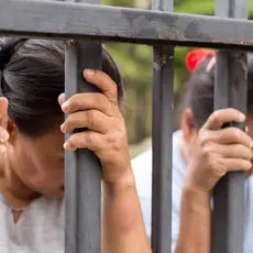 Two women hold onto the bars of a fence