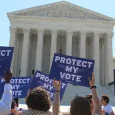 Six people hold up blue signs that read 'protect my vote' at a rally in front of the supreme court