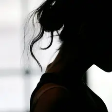 A somber black silhouette of a woman with messy hair looking down.