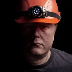 A man wearing an orange hard hat with a headlamp attached