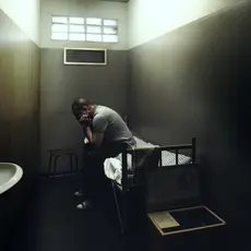 A man in solitary confinement sits on his bed in a small cell.