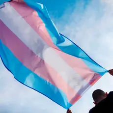 A man holds the transgender flag above his head.