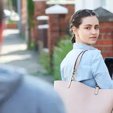 A woman holding her phone looks over her shoulder at the man following her