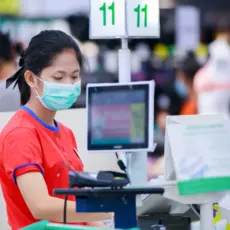 A young grocery store cashier wears a surgical mask while she works.