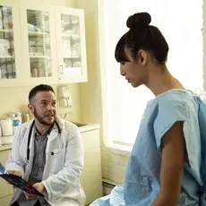 A transgender woman in a hospital gown speaking to her doctor, a