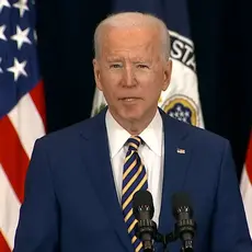 President Joe Biden stands in front of several American flags.