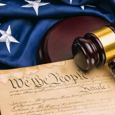 Picture of an American Flag and the U.S. Constitution with the phrase "We The People" clearly visible underneath a gavel.