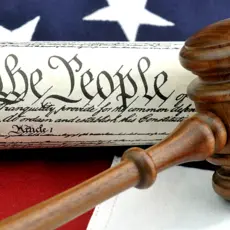 Picture of an American Flag and the U.S. Constitution with the phrase "We The People" clearly visible underneath a gavel.