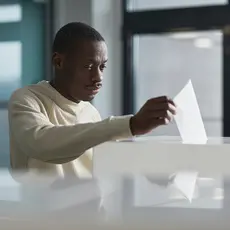 A black man deposits a ballot into a voting box.