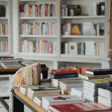 A table full of books in the foreground and shelves of books in the background.