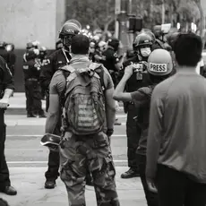 Two Black men and a reporter face a line of police in riot gear.