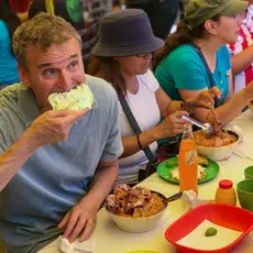 Phil Rosenthal sits at a table with several women eating food.