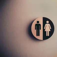 A white wall with a sign showing man and woman symbols seen outside public bathrooms.