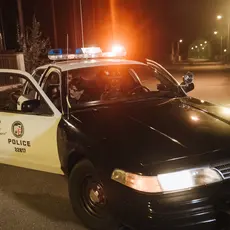 A photo of two police officers in a police car with one person in the back seat.