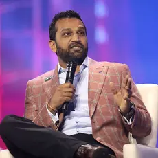 A photo of Kash Patel wearing a pink jacket and holding a microphone.