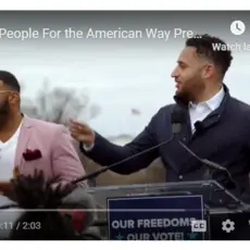 A still of Svante Myrick speaking at a podium with a sign language interpreter next to him.