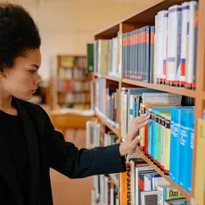 A Black woman looks at a shelf of books in a school library.