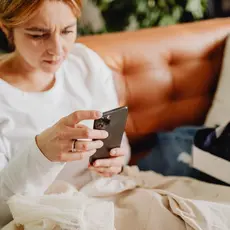 A woman sits on a sofa glaring at her phone.