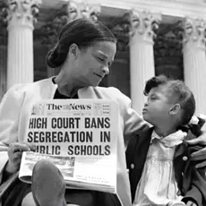 A woman and girl in front of the Supreme Court with a newspaper reading "High Court Bans Segregation in Public Schools"