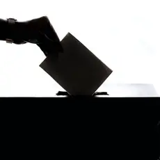 A silhouette of a hand dropping a ballot in a ballot box.