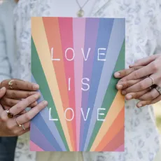 Two people holding a book with "Love is love" and a rainbow design on the cover.