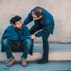 A public safety officer helps a man sitting on a curb.