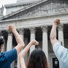 Three people raise their fists outside the Supreme Court building.