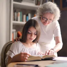 A grandmother helping her granddaughter read a book.