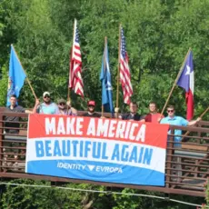 A group of white nationalists holding flags on a bridge.