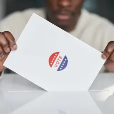 Two hands holding a piece of paper with a sticker that says "Vote"