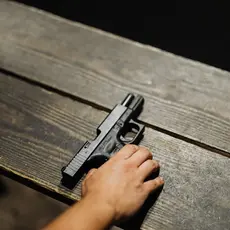 A hand setting a gun on a wooden table.