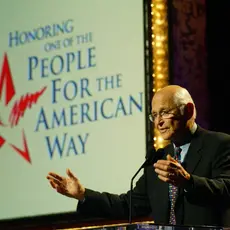 Norman Lear at a podium in front of a sign that reads "People For the American Way"