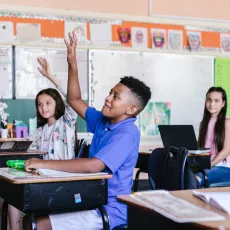 A Black child raising their hand in a classroom