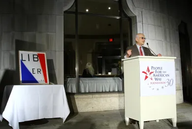 Norman Lear standing at a white podium with a People For the American Way sign on it.