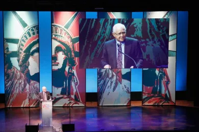 Norman Lear on state with a large video screen and Statue of Liberty background